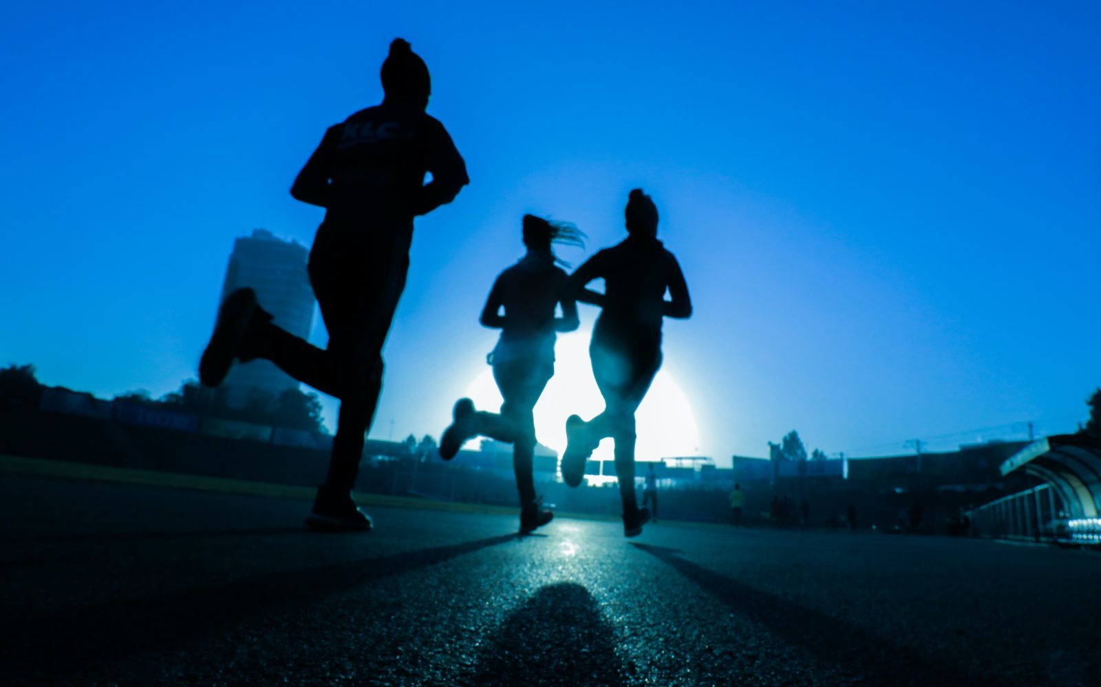 silhouette of three women running on grey concrete road